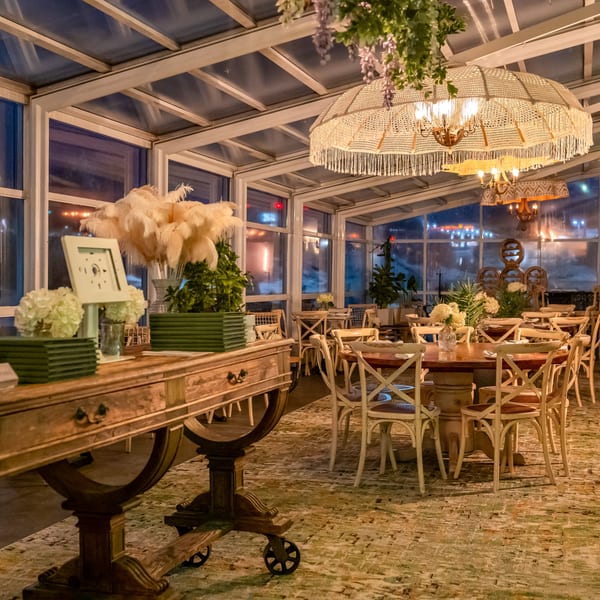 Elegant dining room with glass walls, round tables, white chairs, and decorative lighting.
