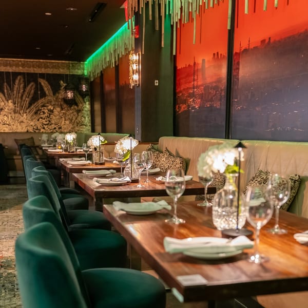 Dining room at Greenhouse Kitchen + Bar with set tables, green velvet chairs, and vibrant wall art.