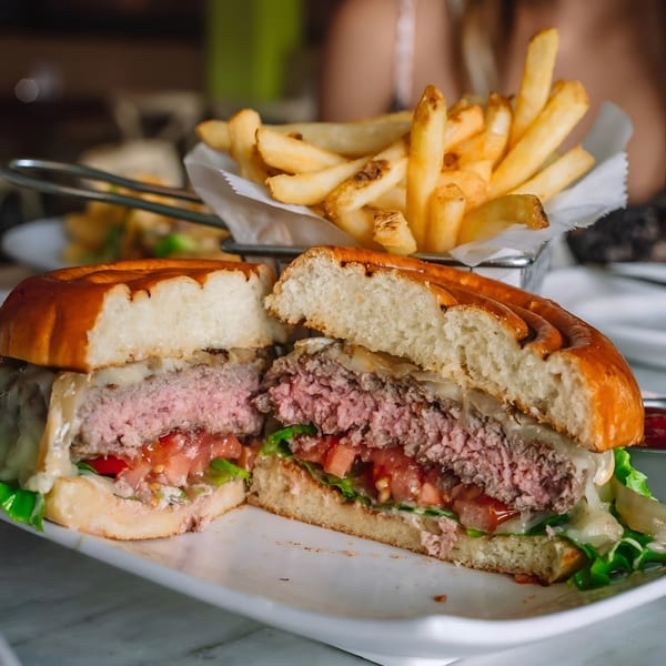 A juicy burger, cut in half, with melted cheese, lettuce, and tomatoes, served with fries.