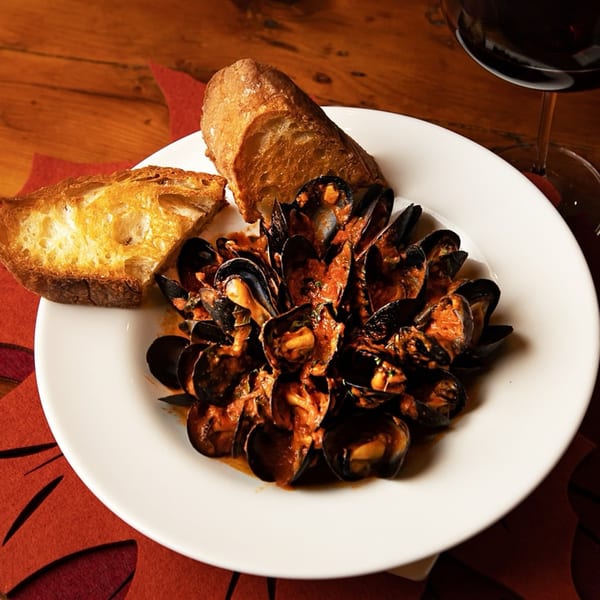 Mussels in a rich red sauce with two pieces of toasted bread and a glass of red wine.