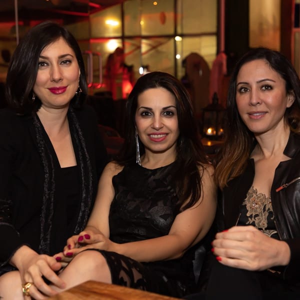 Three women in dark attire smiling at the camera in a dimly lit Greenhouse Kitchen + Bar.