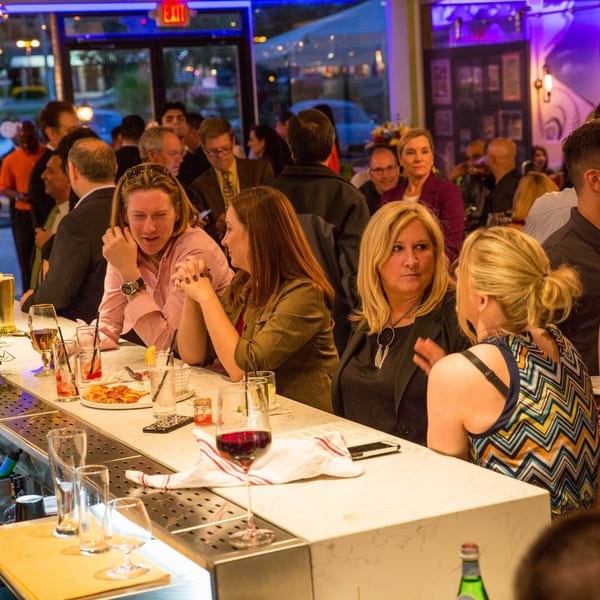 Patrons enjoying drinks and food at the lively bar of Greenhouse Kitchen + Bar.