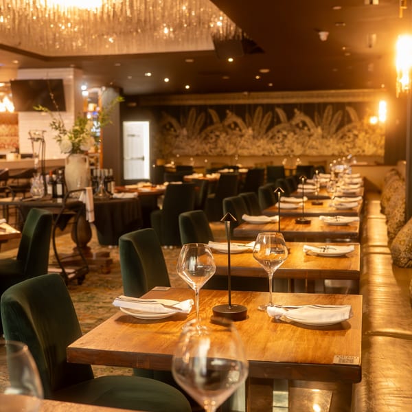 Elegant restaurant interior with wooden tables, green velvet chairs, and a sparkling chandelier.