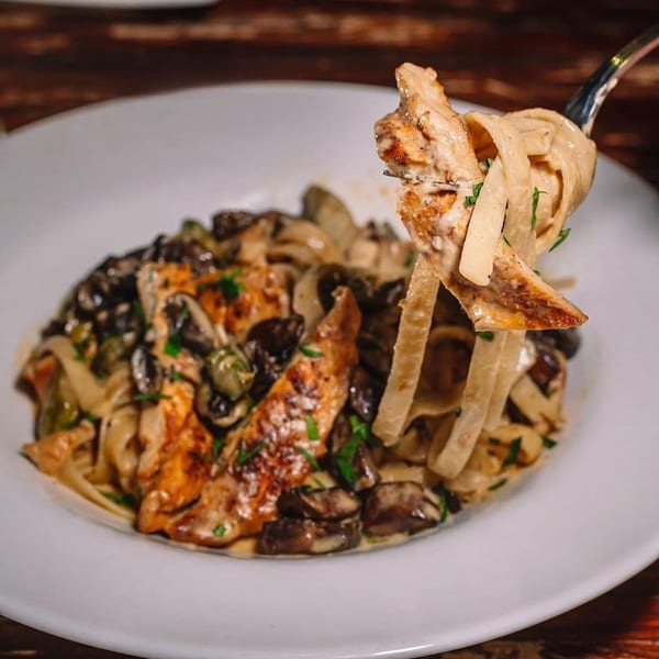 Creamy pasta with grilled chicken, mushrooms, and capers, with a fork lifting a bite.