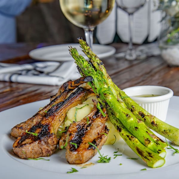 Grilled lamb chops with mashed potatoes and asparagus, served with a side of sauce and white wine.