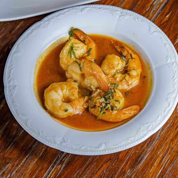 Shrimp in a rich orange sauce, garnished with herbs, served in a white bowl on a wooden table.