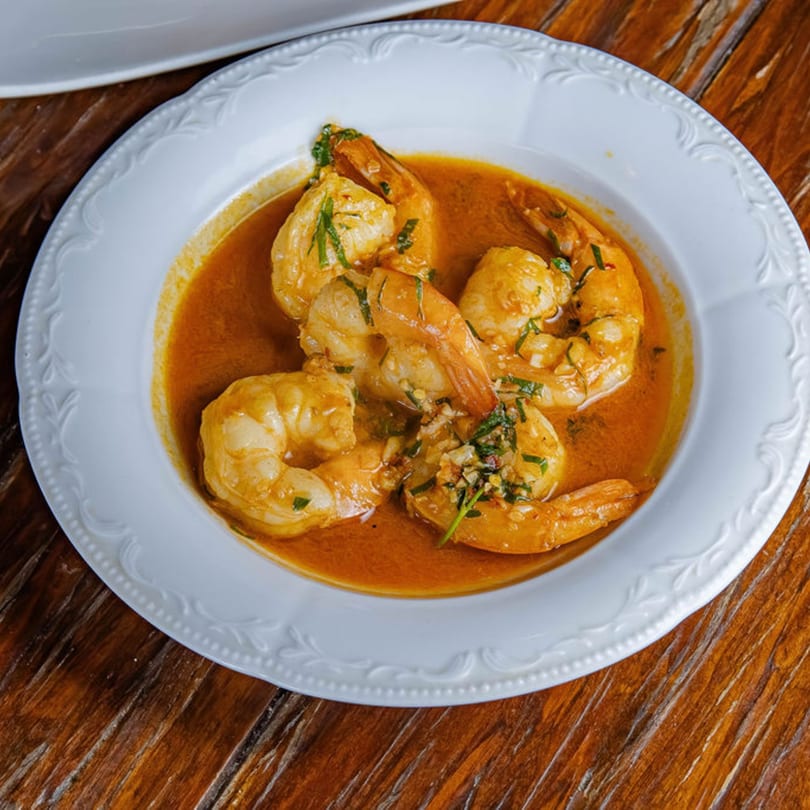 Shrimp in a rich orange sauce, garnished with herbs, served in a white bowl on a wooden table.