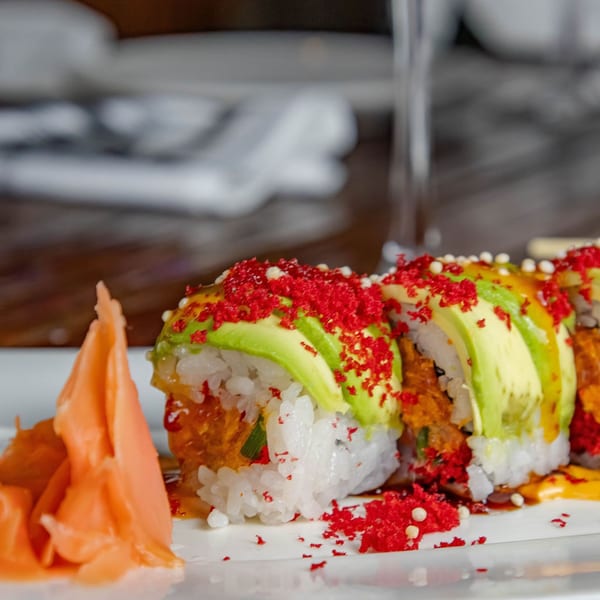 Sushi rolls topped with avocado, red roe, and sauce, served with pickled ginger.