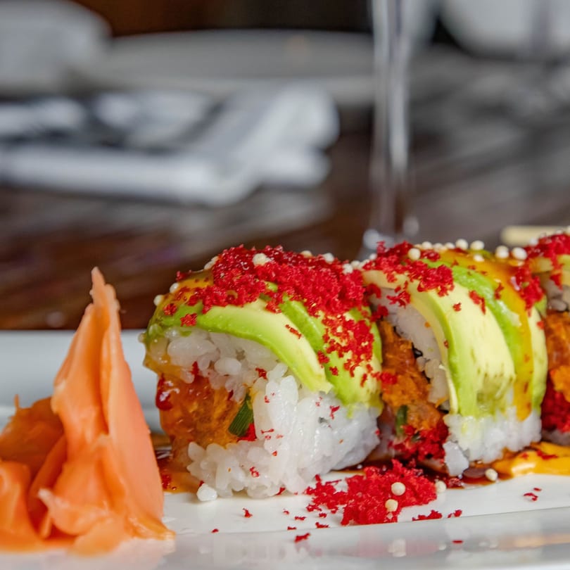 Sushi rolls topped with avocado, red roe, and sauce, served with pickled ginger.
