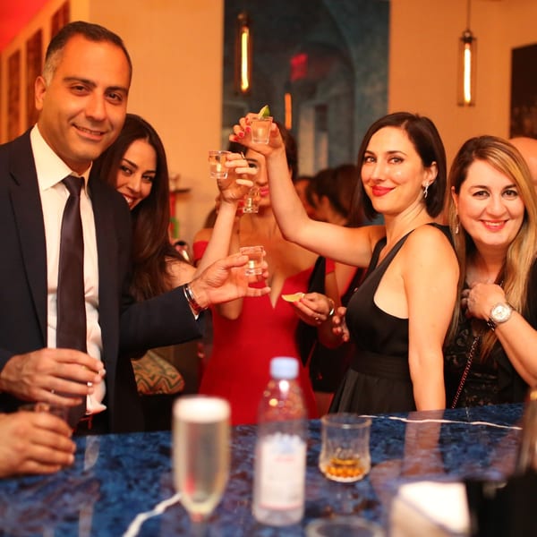 Guests at Greenhouse Kitchen + Bar raising shot glasses in a toast, smiling at the camera.