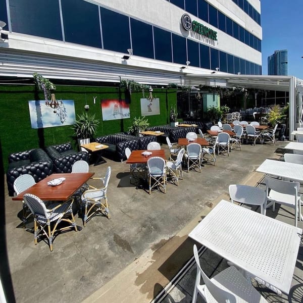 Greenhouse Kitchen + Bar's outdoor patio with various seating arrangements, including black leather sofas and white chairs.