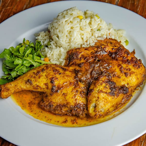 A plate of roasted chicken with rice and a side salad, drizzled with sauce.