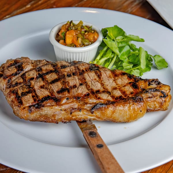 Grilled steak with char marks, a side of green salad, and a small dish of relish on a white plate.