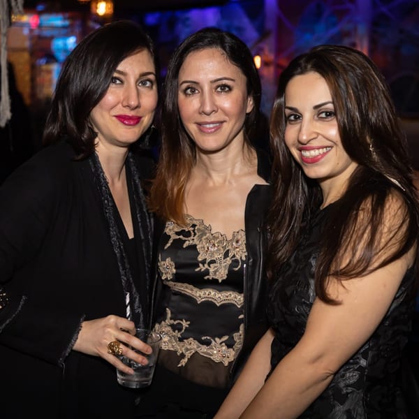 Three women smiling at the camera, one holding a drink, in a dimly lit Greenhouse Kitchen + Bar.