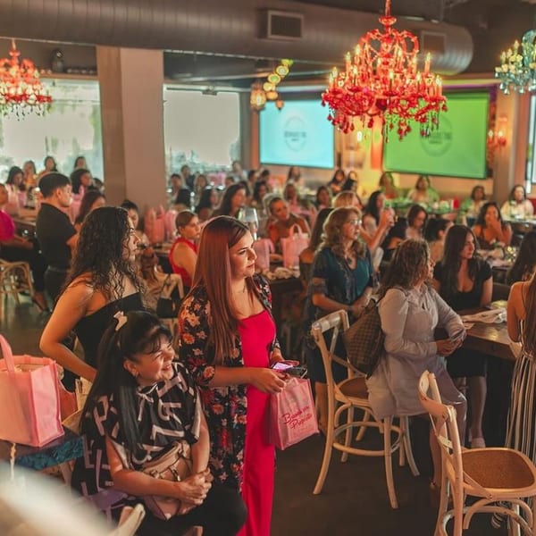 A large group of people, mostly women, gathered in a restaurant with red chandeliers and screens.
