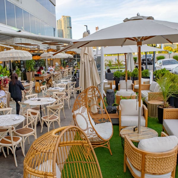 Outdoor restaurant patio with various seating, umbrellas, and lush greenery under a modern building.