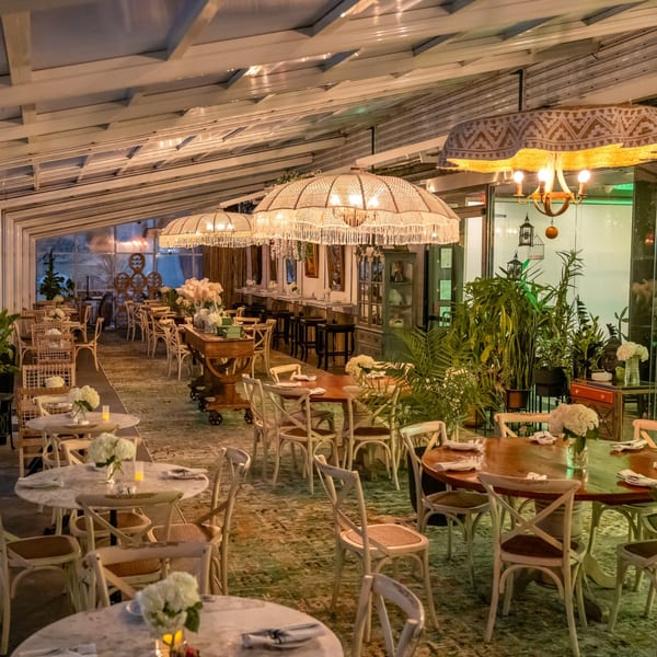 Greenhouse Kitchen + Bar's Asian-fusion restaurant interior with tables, chairs, plants, and decorative lighting.