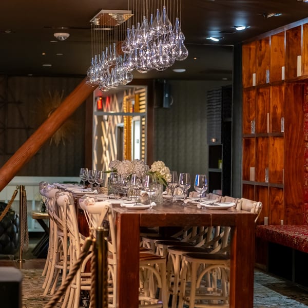 A long dining table set with glasses and white flowers under a modern teardrop chandelier.