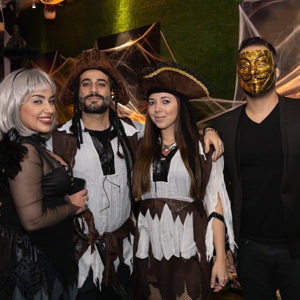 Four people in Halloween costumes, including pirates and a gold mask, posing together at Greenhouse Kitchen + Bar.