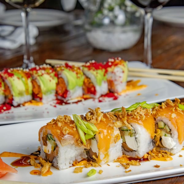 Two plates of colorful sushi rolls, one with avocado and red roe, the other with crispy onions.
