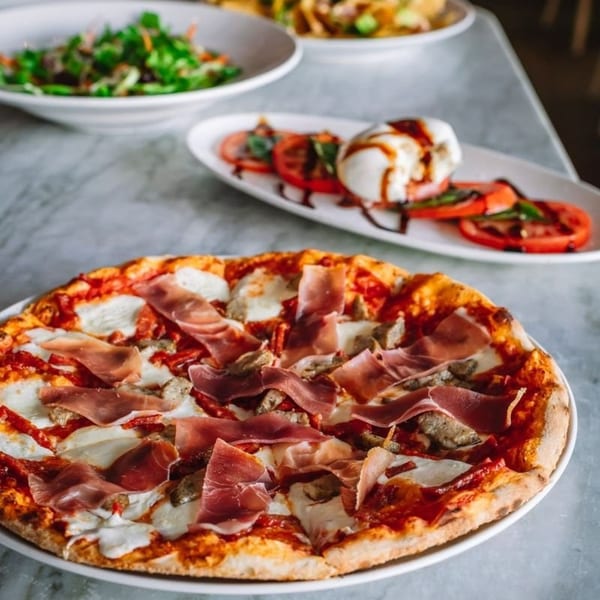 A prosciutto and mushroom pizza with mozzarella, alongside a caprese salad and green salad.